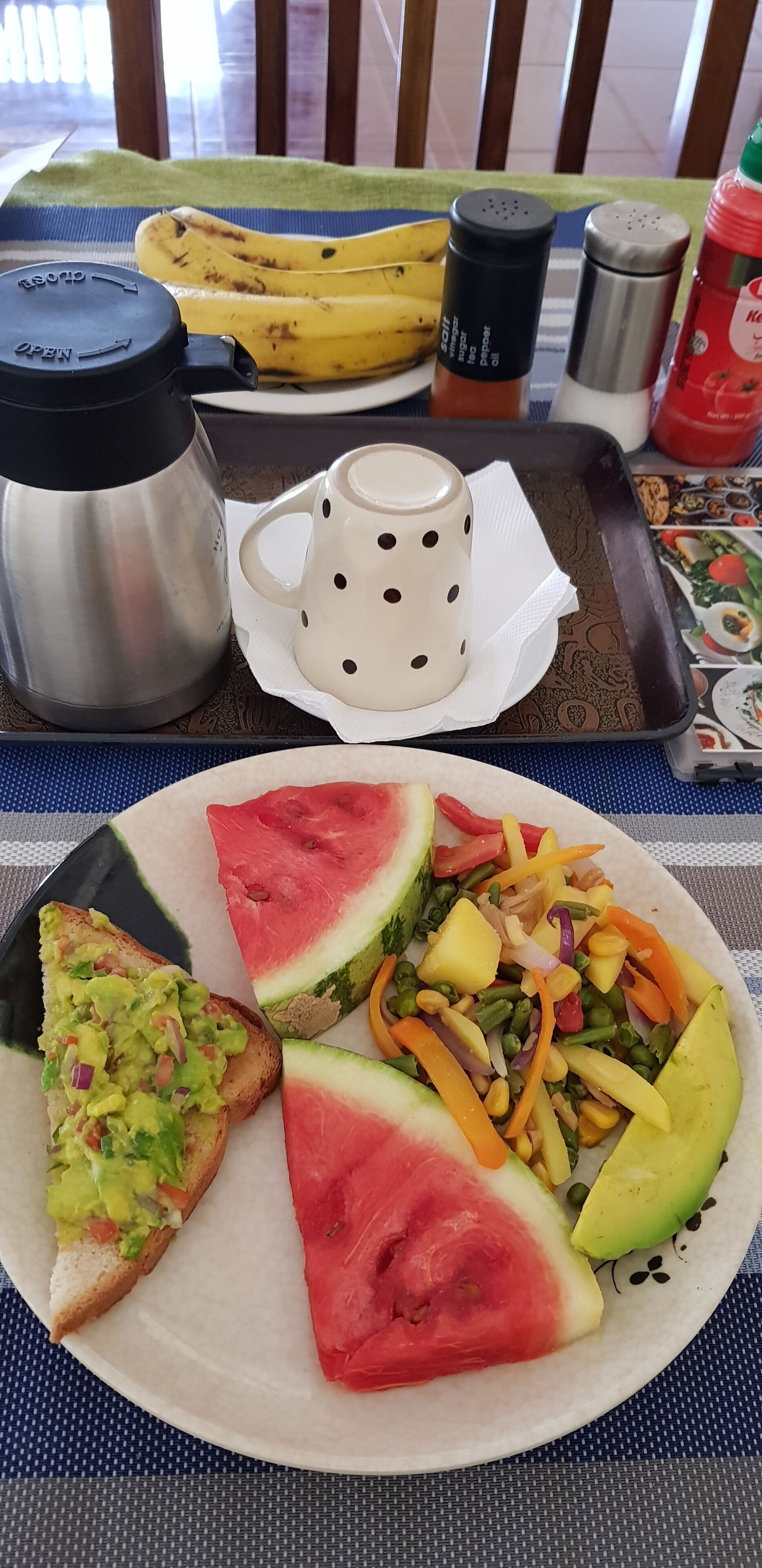 Una mesa con un plato de comida, un termo, una taza y salsas.