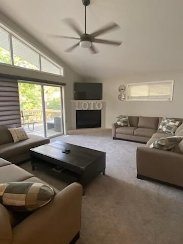 A spacious living room with a large window, a fireplace, and a ceiling fan.