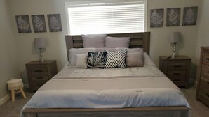Un dormitorio con una cama grande, dos mesitas de noche, una ventana con persianas y decoración en la pared.