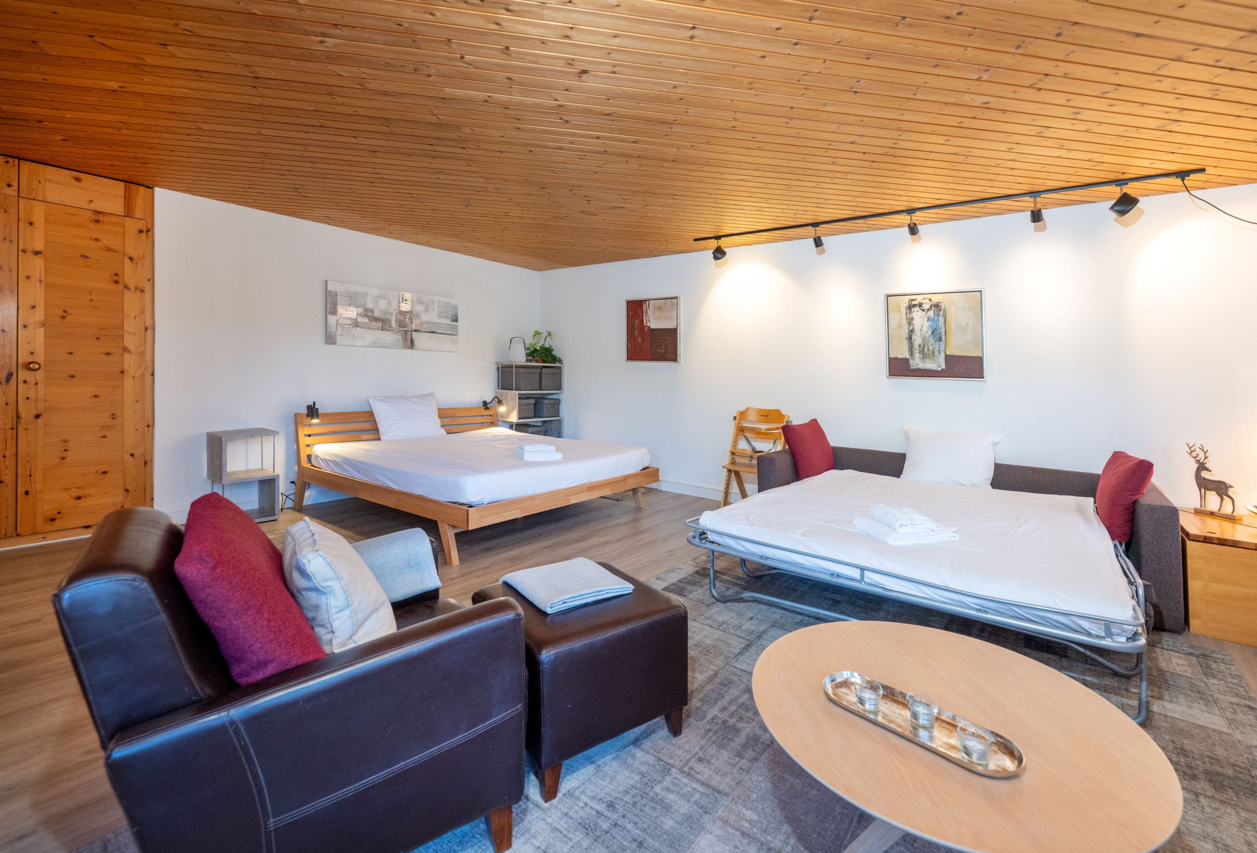 Una moderna camera d'albergo con soffitto in legno, due letti, un divano, un tavolino da caffè e opere d'arte alle pareti.