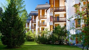 A row of multi-story buildings with balconies, surrounded by greenery and trees. - Apartment with mountain view and spa access (Lenzerheide/Lai)