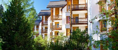 Una hilera de edificios de varios pisos con balcones, rodeados de vegetación y árboles.