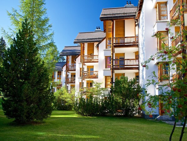 Une rangée d’immeubles à étages, dotés de balcons, et entourés de verdure et d’arbres.