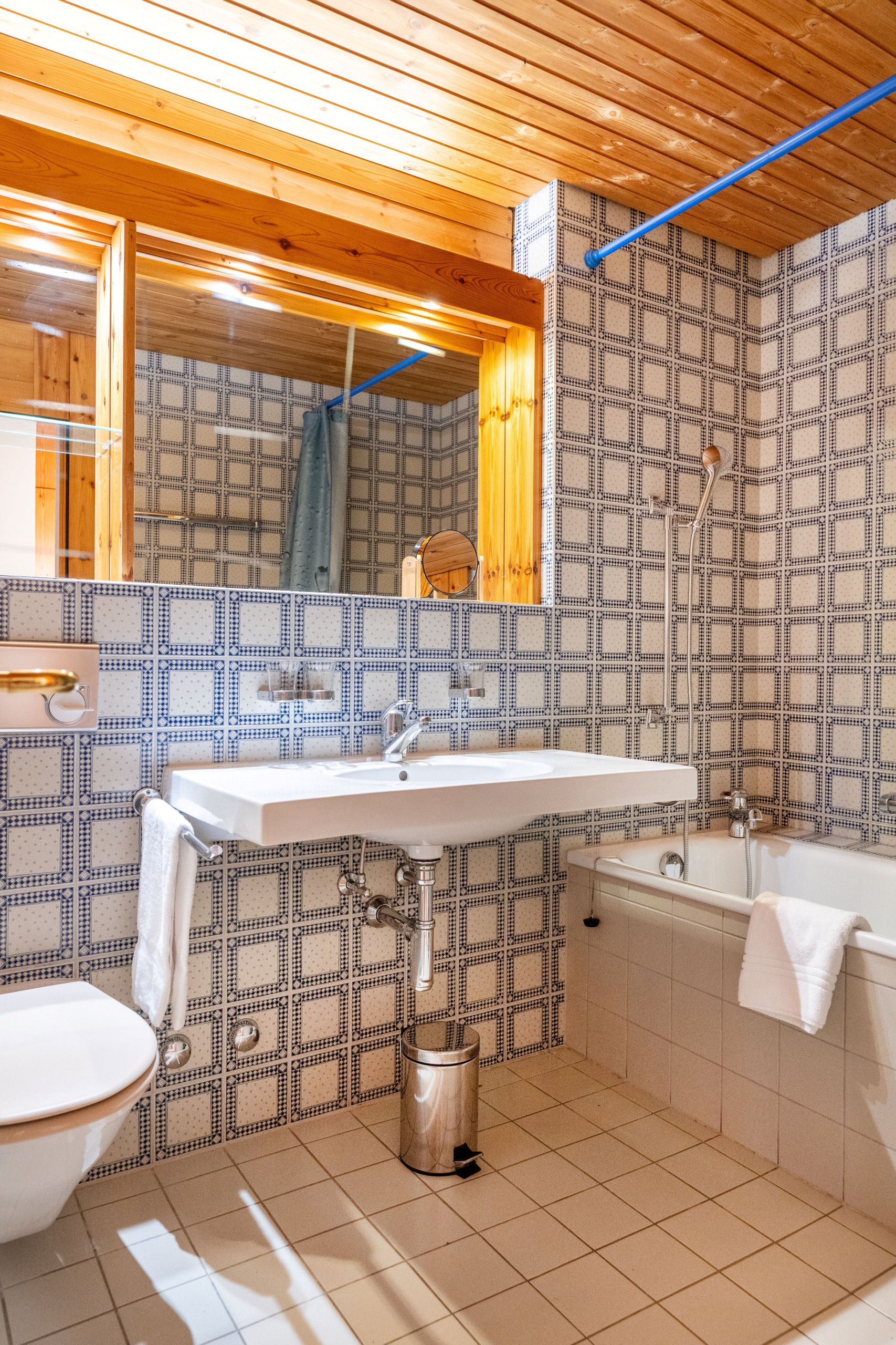 Een badkamer met een houten plafond, patroontegels, een wastafel, een toilet en een bad.