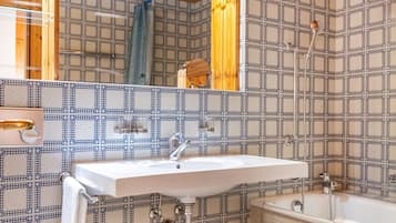 Een badkamer met een houten plafond, patroontegels, een wastafel, een toilet en een bad.