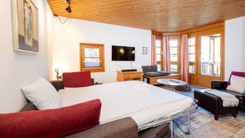 Una camera d'albergo con un letto, una scrivania, una televisione, un divano e una finestra con tende.