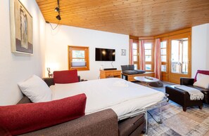 Une chambre d’hôtel avec un lit, un bureau, une télévision, un canapé et une fenêtre avec des rideaux.