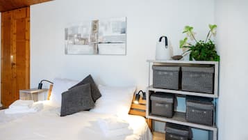 A bedroom with a bed, pillows, a bedside table, a lamp, a wall art piece, a plant, and storage baskets.