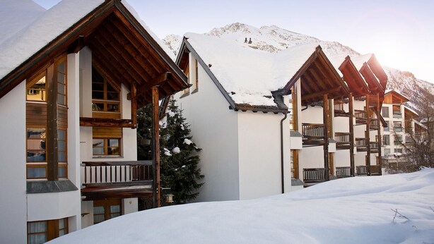 A snow-covered building with wooden balconies and a mountain backdrop. - Apartment with mountain view and spa access (Lenzerheide/Lai)