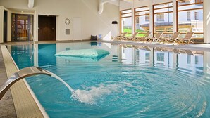 An indoor swimming pool with clear water, a diving board, and lounge chairs by the windows. - Apartment with mountain view and spa access (Lenzerheide/Lai)