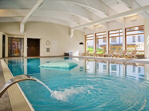 An indoor swimming pool with clear water, a diving board, and lounge chairs by the windows.