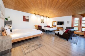 A modern room with a wooden ceiling, a bed, a sofa, a TV, and a window with curtains.