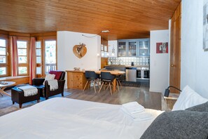 Una habitación acogedora con cama, una mesa de comedor con sillas, una zona de cocina y un amplio ventanal con cortinas.