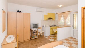 Habitació senzilla amb rentaplats, armari de fusta, televisió i taula petita amb una cadira.