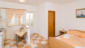 Un dormitori amb un terra de petxines, un llit amb edredó taronja, una porta de fusta, una finestra amb cortines i un quadre al mur.