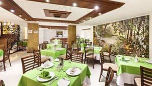 Een restaurant met groene tafelkleden, houten stoelen en een muurschildering van een bos.