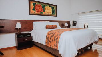 A neatly made bed with a patterned throw, a nightstand with a lamp, and a painting of flowers on the wall.
