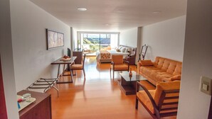 Een moderne woonkamer met een bank, salontafel en stoelen. Er is een eethoek met een tafel en stoelen. De kamer heeft grote ramen met uitzicht op het landschap.