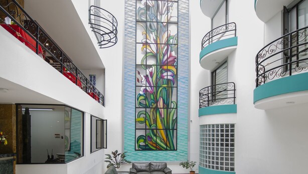 Een ruime atrium met een centraal geplaatst glas-in-loodkunstwerk, diverse zithoeken en een trap naar de bovenverdiepingen.
