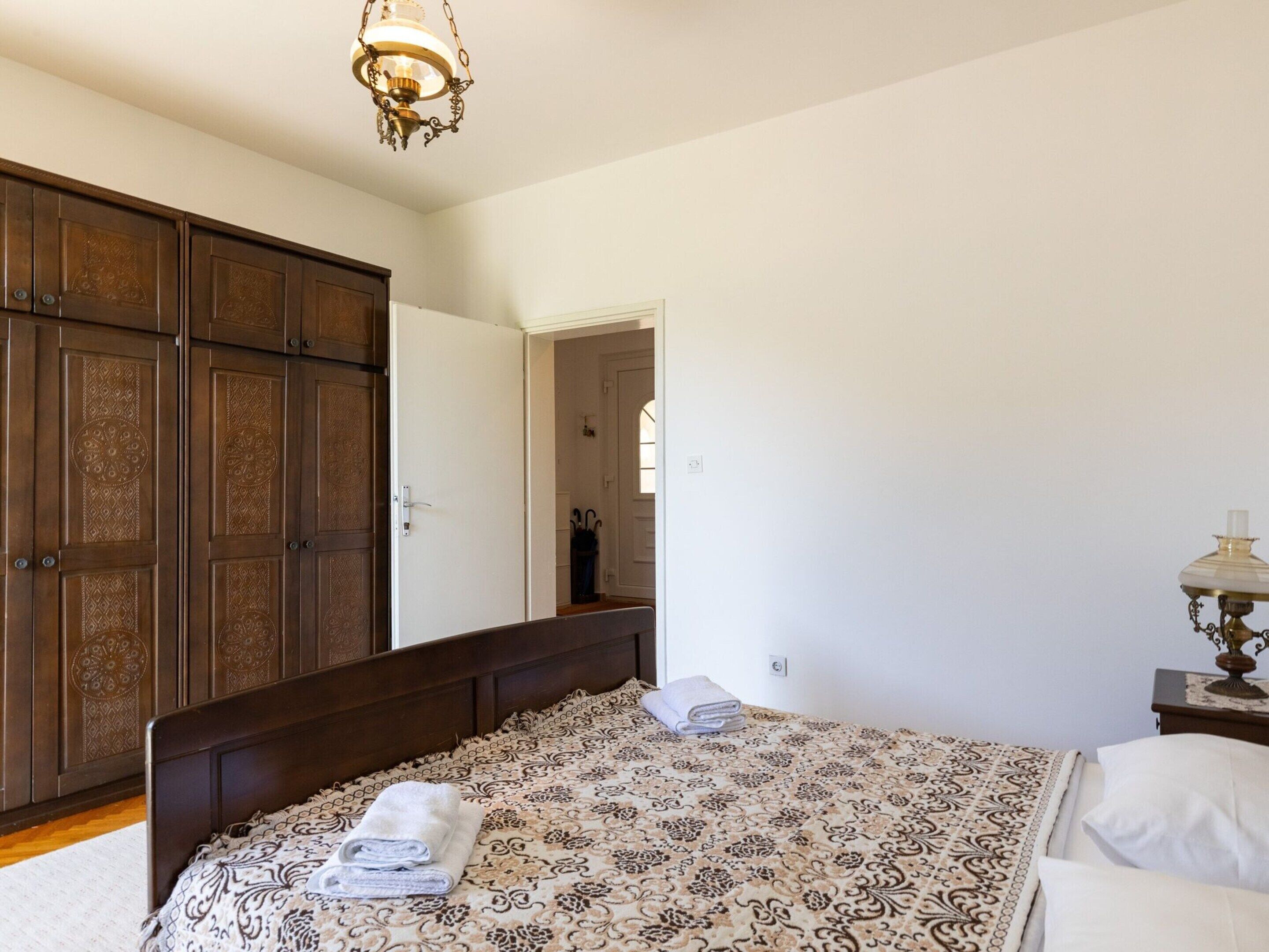 A bedroom with a large bed, a wardrobe, a nightstand, and a chandelier.