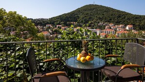 A balcony with two chairs and a table, a view of a hillside town, and a clear sky. - Begovic Guest House - Two-bedroom Suite With Balcony (Dubrovnik)