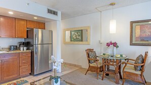 A modern kitchen with wooden cabinets, a stainless steel refrigerator, and a dining area with wicker chairs and a glass table. -   Dlx OCEANVIEW Maui  Studio..Updated!
West Maui. AC. Royal Kahana. (Lahaina)