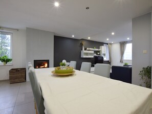 Uma sala de estar moderna com lareira, mesa de jantar e área de cozinha com armários e televisão.