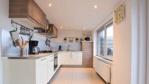 Een moderne keuken met witte kasten, roestvrijstalen apparatuur en een raam dat voor daglicht zorgt.