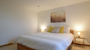 Een slaapkamer met een houten bed, twee nachtkastjes met lampen, en een kunstwerk aan de wand.