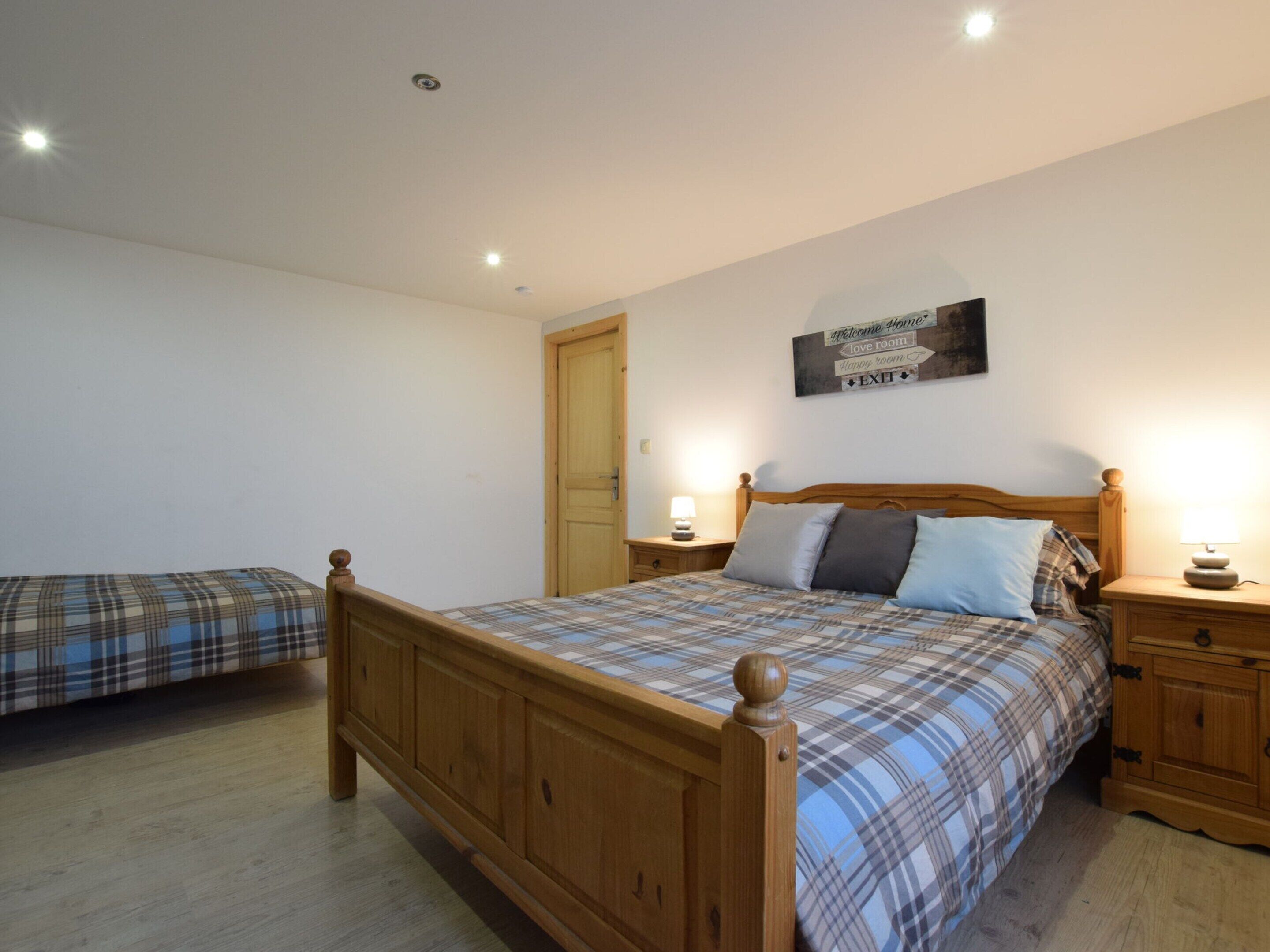A bedroom with a wooden bed, a nightstand, a wall-mounted sign, and a door.