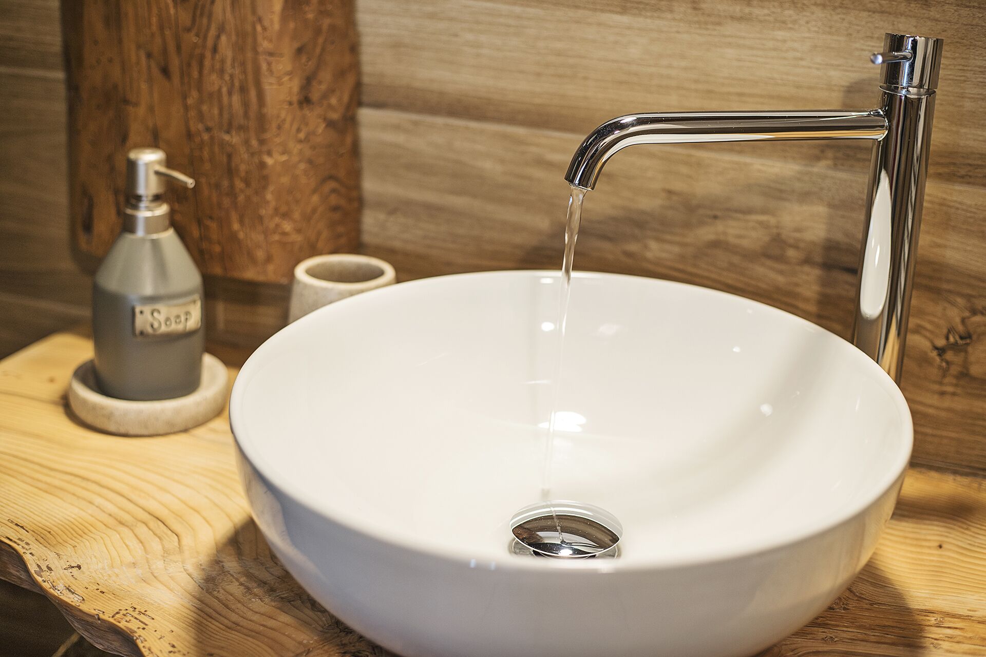 A white ceramic sink with a single faucet, a soap dispenser, and a cup on a wooden countertop.