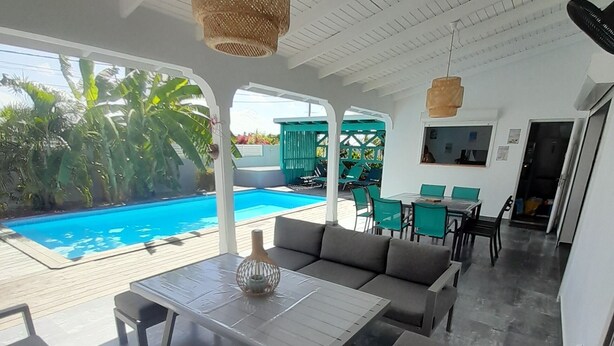 A modern outdoor lounge area with a pool, grey sofas, a table, and hanging lights.