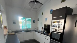 A modern kitchen with dark grey cabinets, a black countertop, and a stainless steel refrigerator. There is a window with a view of greenery outside.