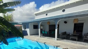 A poolside area with a wooden deck, a pool, and a building with a white exterior and blue accents.