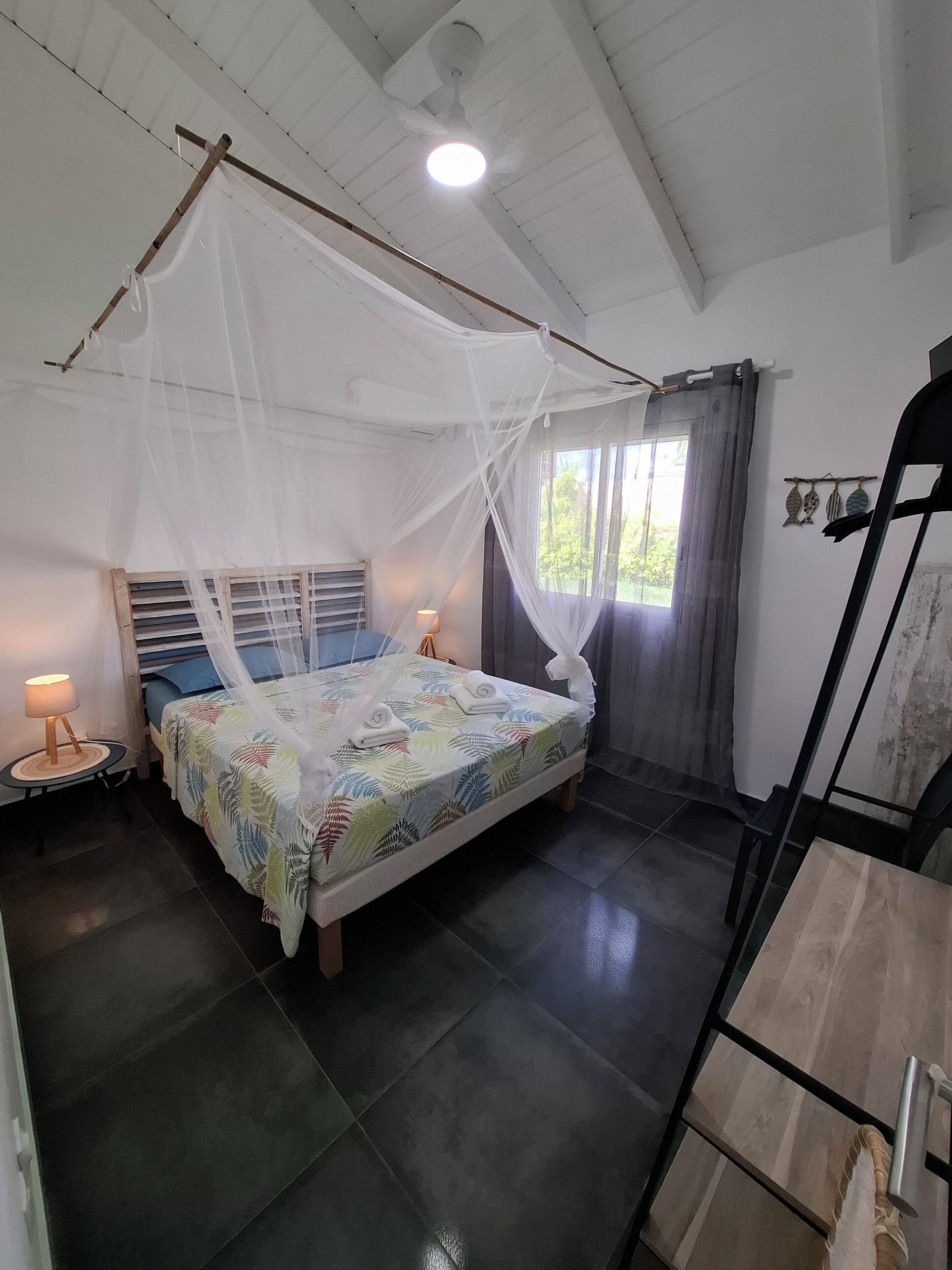 A bedroom with a bed under a mosquito net, a bedside lamp, and a window with curtains.