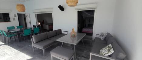 A modern living room with a sofa, dining table, and chairs. There is a large window allowing natural light to enter.