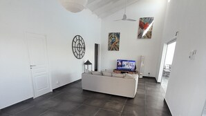 A spacious living room with a large dark tile floor, a white sofa, a television, and a ceiling fan.