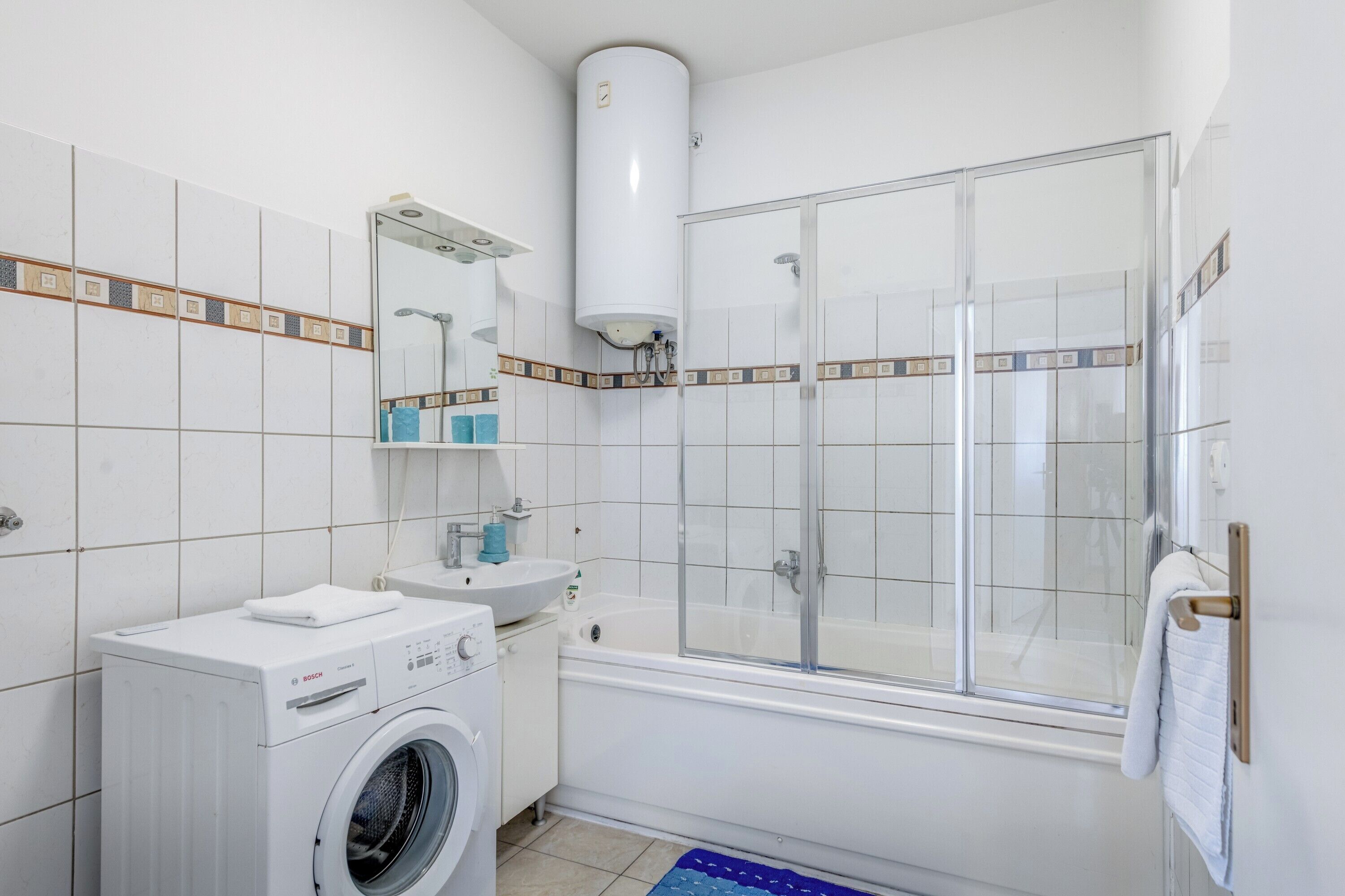 A modern bathroom with a Bosch washing machine, a sink, a mirror, and a glass-enclosed shower.