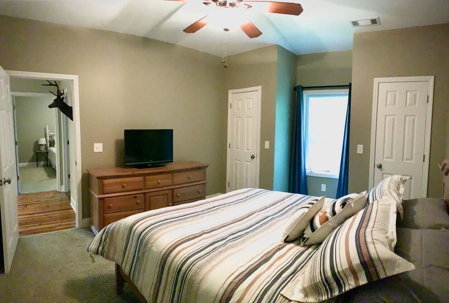 Un dormitorio con cama, cómoda, televisor y puerta que da a otra habitación.