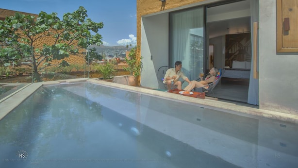 Een modern huis met een overdekt zwembad, een schuifpui en uitzicht op een boom en verre bergen.