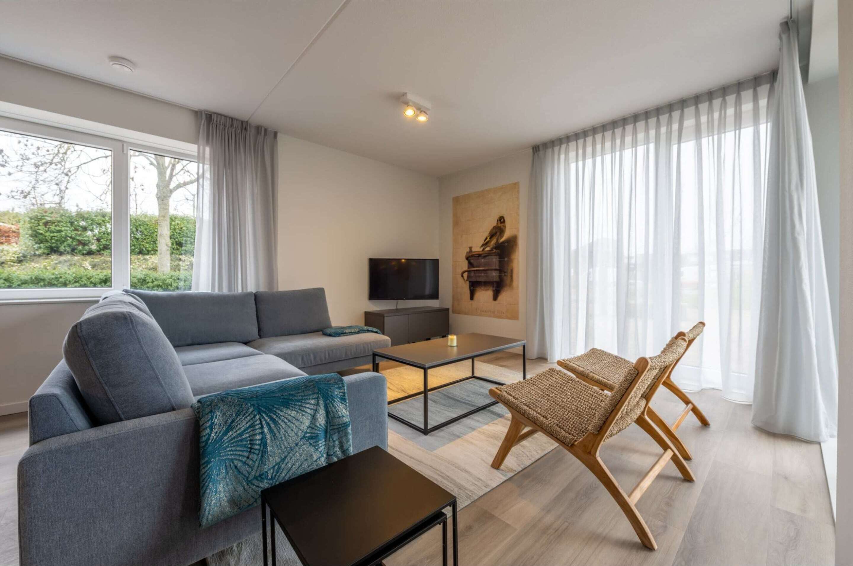Un salon moderne avec un canapé gris, une table basse, un téléviseur et un tableau accroché au mur.