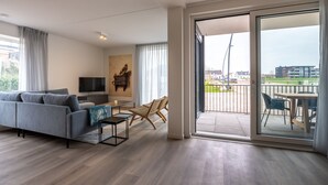 Ein modernes Wohnzimmer mit Sofa, Fernseher und einem Balkon mit Sitzgelegenheit.