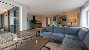 Ein modernes Wohnzimmer mit einer grauen Couch, Korbstühlen, einem Couchtisch und einem Essbereich mit Tisch und Stühlen.