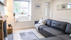 A modern living room with a grey sofa, a small rug, and a wooden side table with a bottle and a box. - 4 Railway Terrace (Conwy)