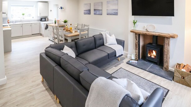 A modern living room with a grey sectional sofa, a fireplace, and a flat-screen TV mounted on the wall. - 4 Railway Terrace (Conwy)