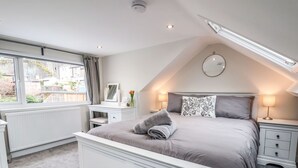 A bedroom with a bed, bedside tables, a dresser, a vanity with a mirror, and a window with curtains. - 4 Railway Terrace (Conwy)