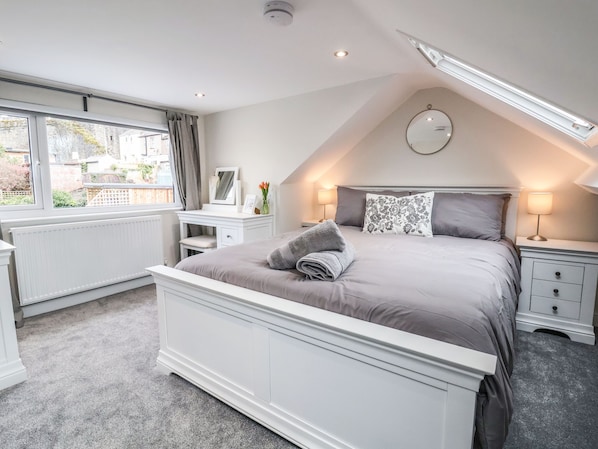 Une chambre à coucher comprenant un lit, des tables de chevet, une commode, une coiffeuse avec un miroir et une fenêtre avec des rideaux.