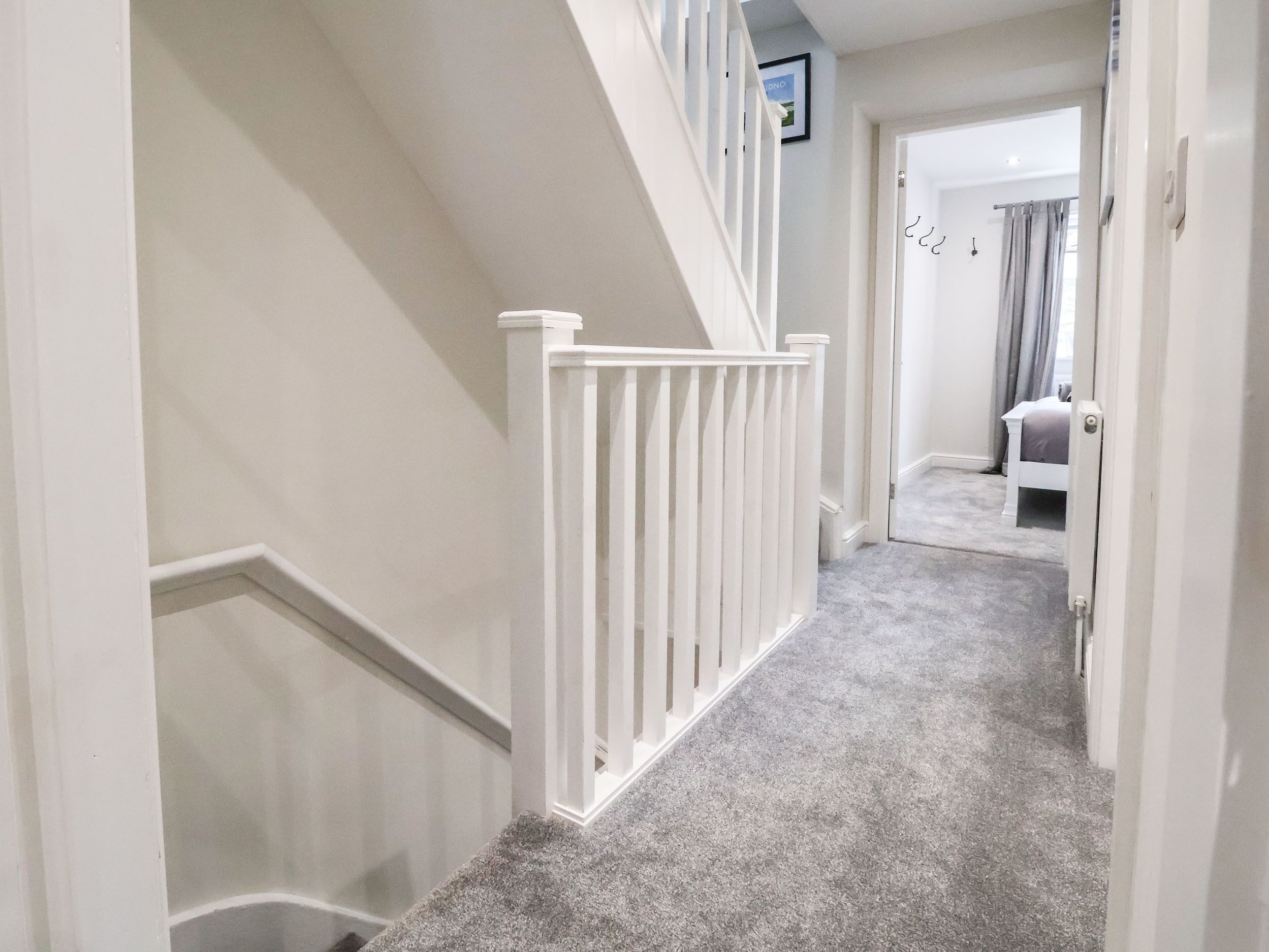 A carpeted hallway with a white railing and a door leading to a bedroom.