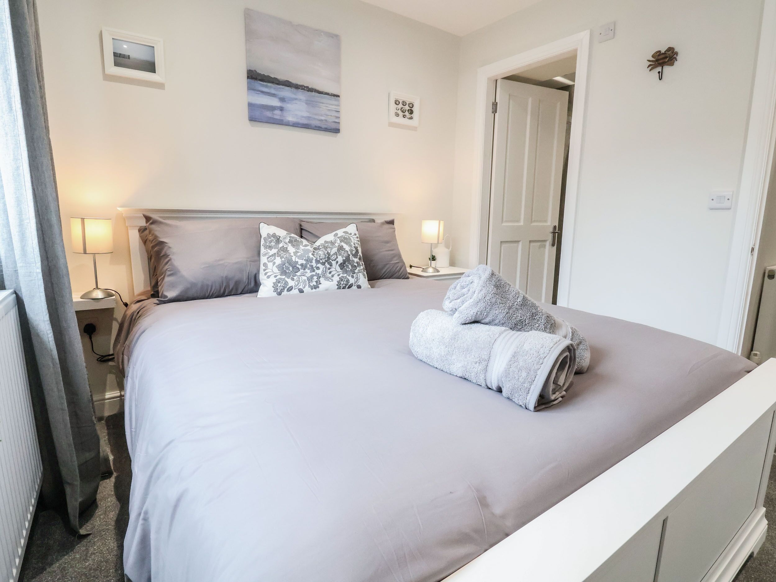A neatly made bed with a grey blanket and two pillows, a bedside lamp, and a framed picture on the wall.
