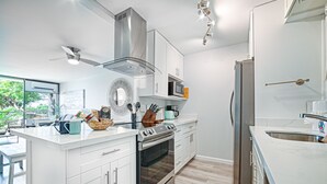 A modern kitchen with white cabinetry, stainless steel appliances, and a large island. - Ocean view, fully remodeled, 2nd floor, few steps away from the best beaches (Kihei)